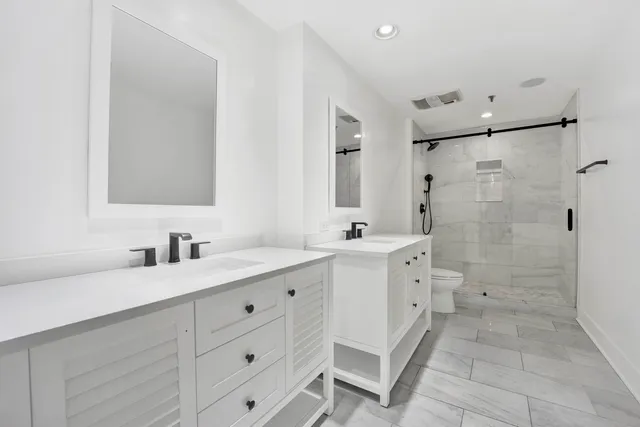 a spacious bathroom with a double vanity sink toilet mirror and shower