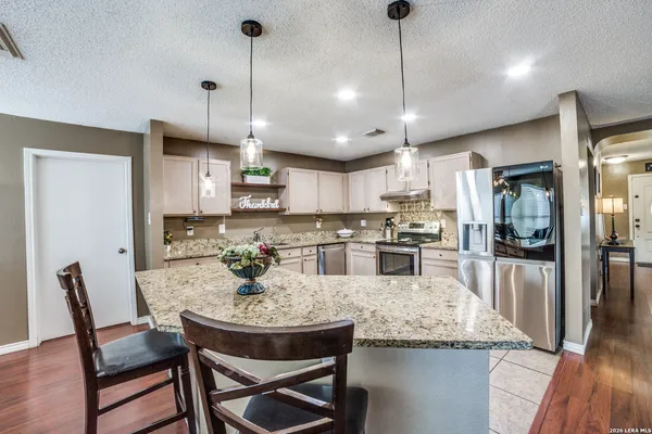 a kitchen with stainless steel appliances granite countertop a sink a stove a kitchen island with chairs and white cabinets