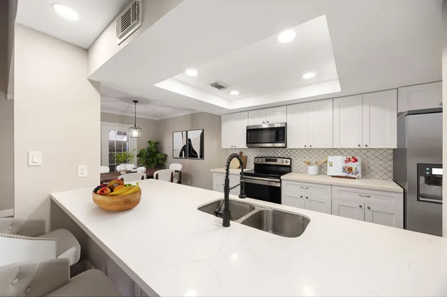 a kitchen with stainless steel appliances a sink a stove top oven a dining table and chairs with white cabinets