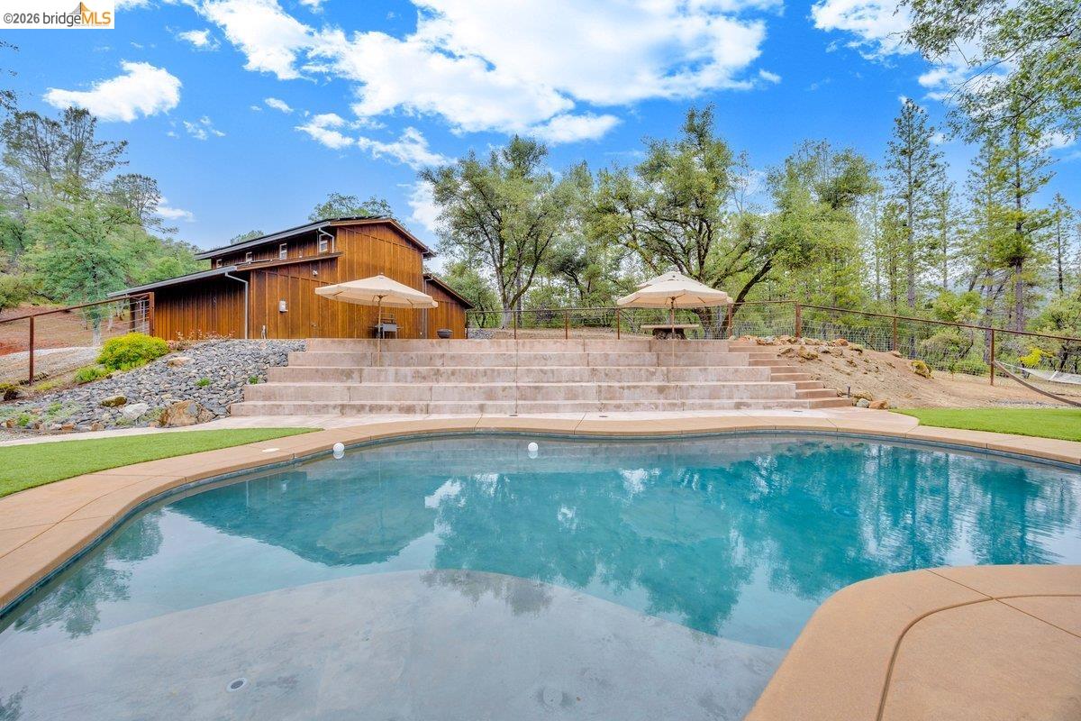 21950 Lyons Bald Mountain Road Sonora, CA 95370 - Photo 55 of 76 Curved swimming pool with a broad coping, artificial turf surrounds, and terraced hardscaping