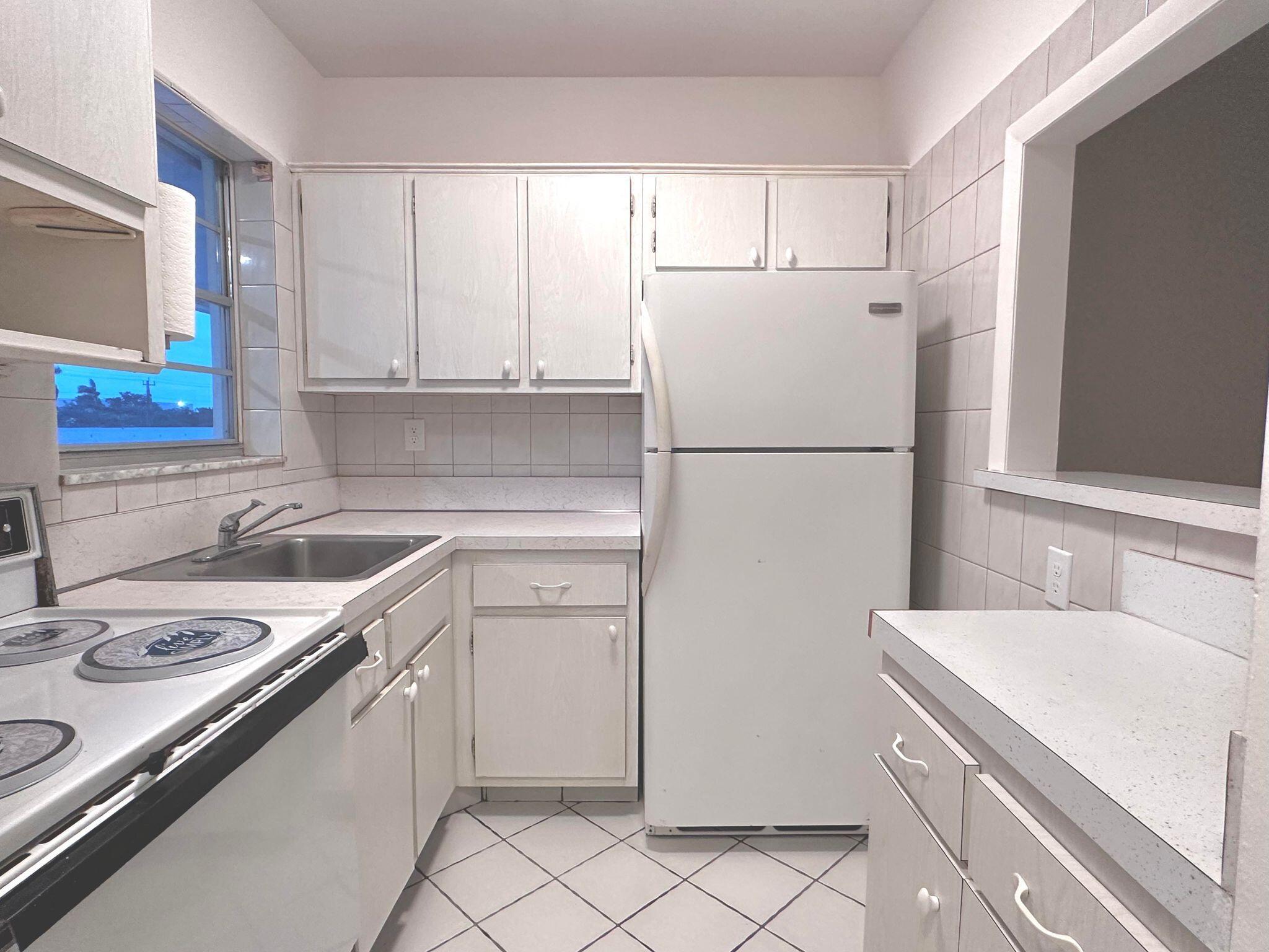 a white kitchen with sink refrigerator and cabinets