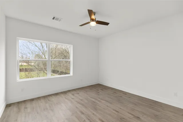 an empty room with wooden floor chandelier and windows
