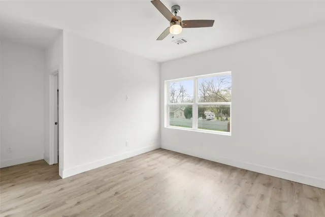 an empty room with wooden floor chandelier fan and windows