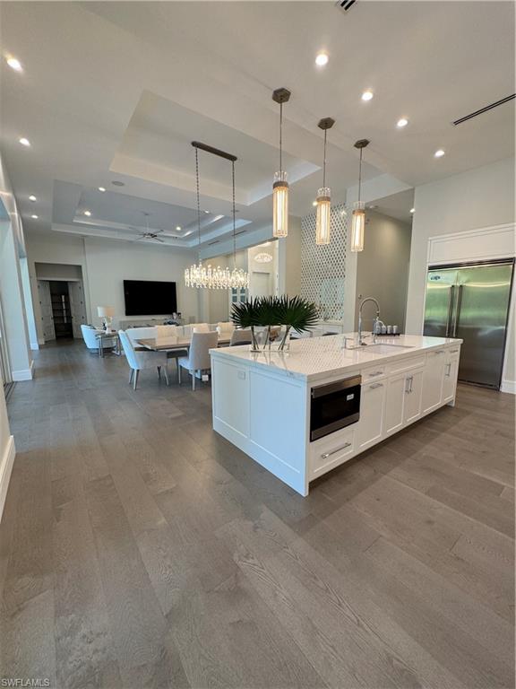 569 Neapolitan Way Naples, FL 34103 - Photo 50 of 50 Kitchen featuring open floor plan, fridge, white cabinetry, a raised ceiling, and a kitchen island with sink