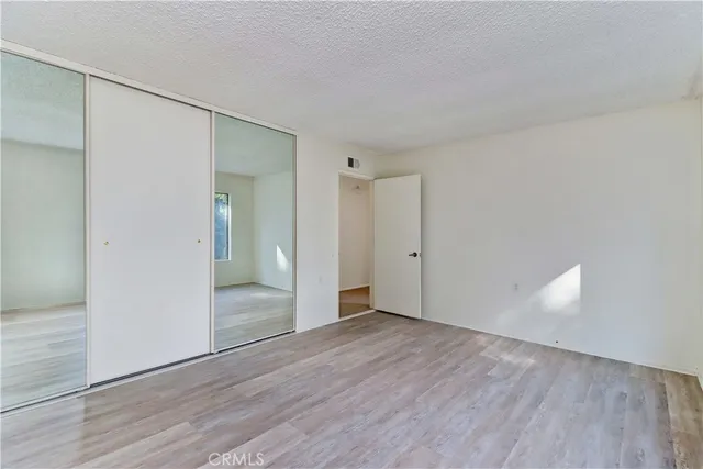 a view of an empty room with wooden floor & mirror