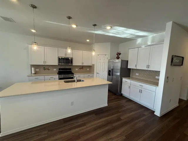 a large white kitchen with wooden floor and stainless steel appliances