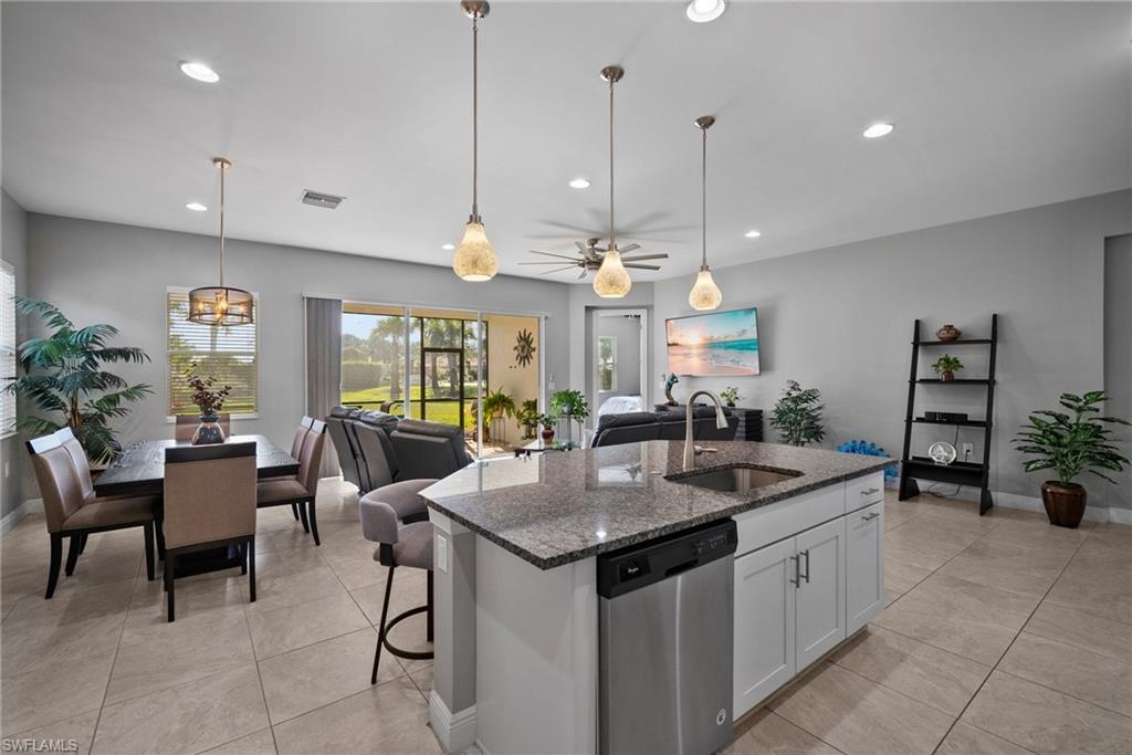 Kitchen featuring stainless steel dishwasher, dark stone counters, a kitchen island with sink, sink, and white cabinets