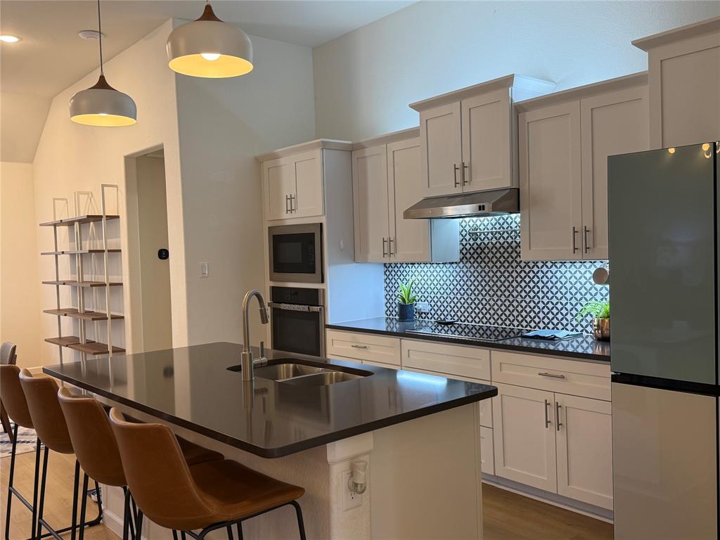 1122 Silverthorne Trail Justin, TX 76247 - Photo 4 of 19 Kitchen with freestanding refrigerator, decorative backsplash, oven, hanging light fixtures, and a center island with sink