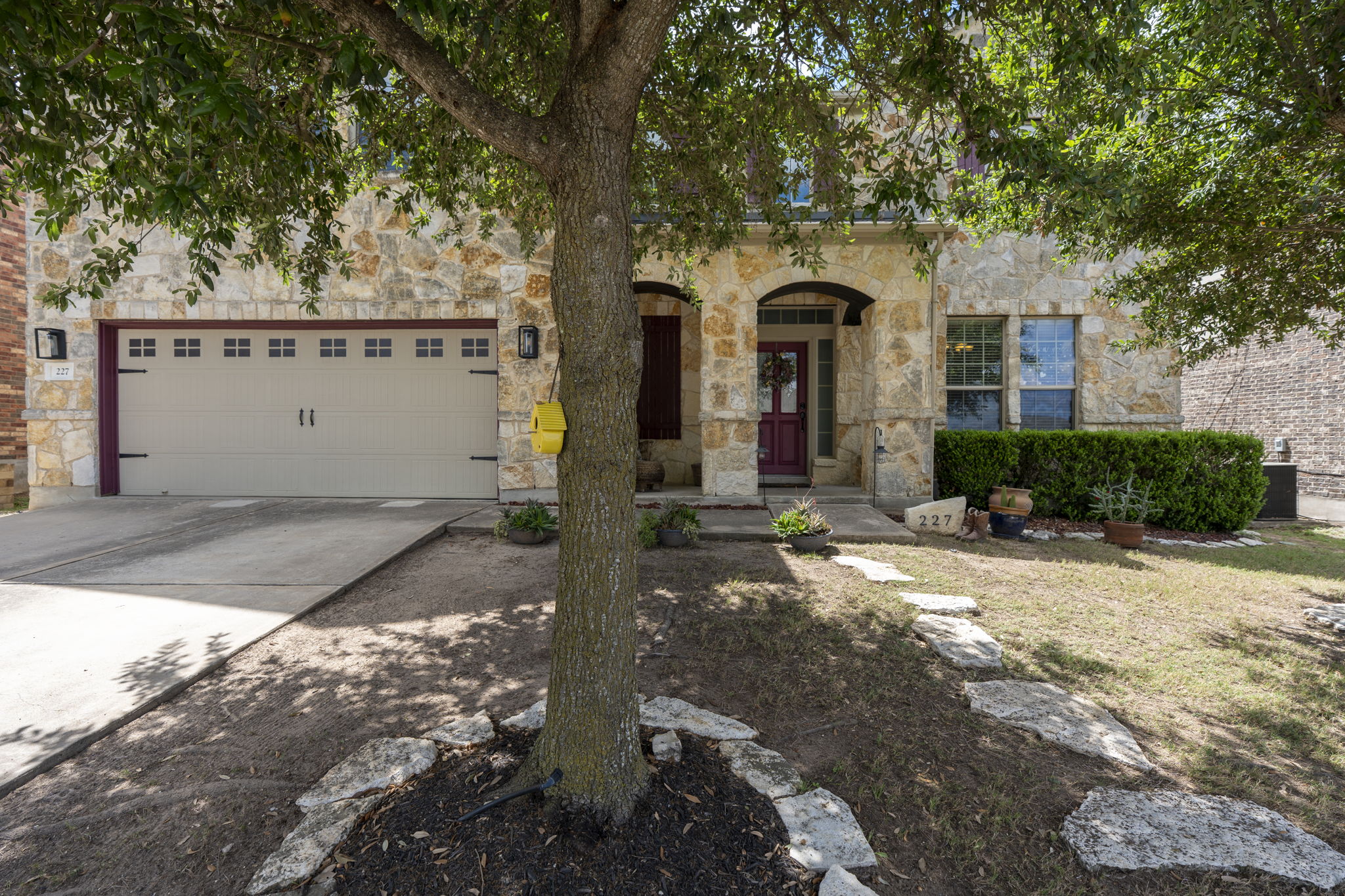 227 Sandstone Trail Buda, TX 78610 - Photo 2 of 33 Stone facade residence featuring a two-car garage with decorative hardware, an arched entry, a red-hued front door, and a stone-lined pathway
