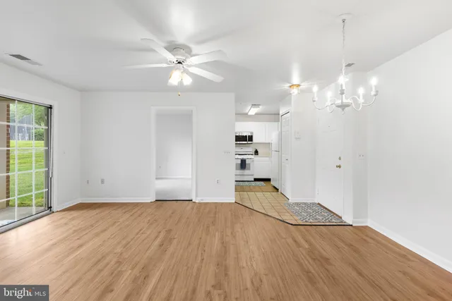 a view of an empty room with wooden floor and a kitchen