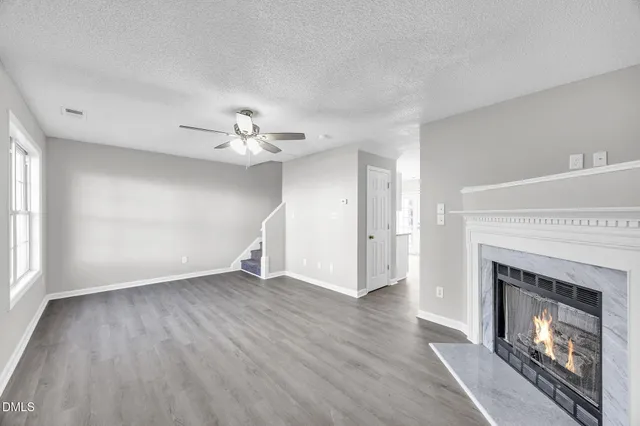 a view of an empty room with wooden floor fireplace and a window