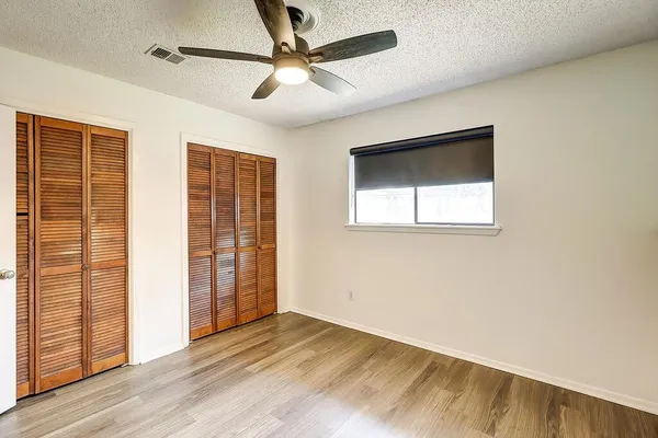 an empty room with wooden floor fan and windows
