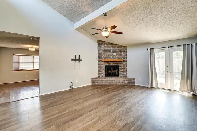 an empty room with wooden floor fireplace and windows