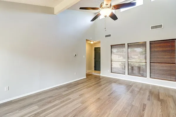 an empty room with wooden floor fan and windows