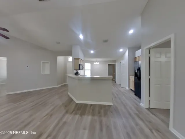 a view of kitchen and empty room with wooden floor