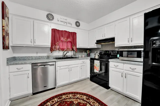 a kitchen with granite countertop a sink cabinets stainless steel appliances and a window