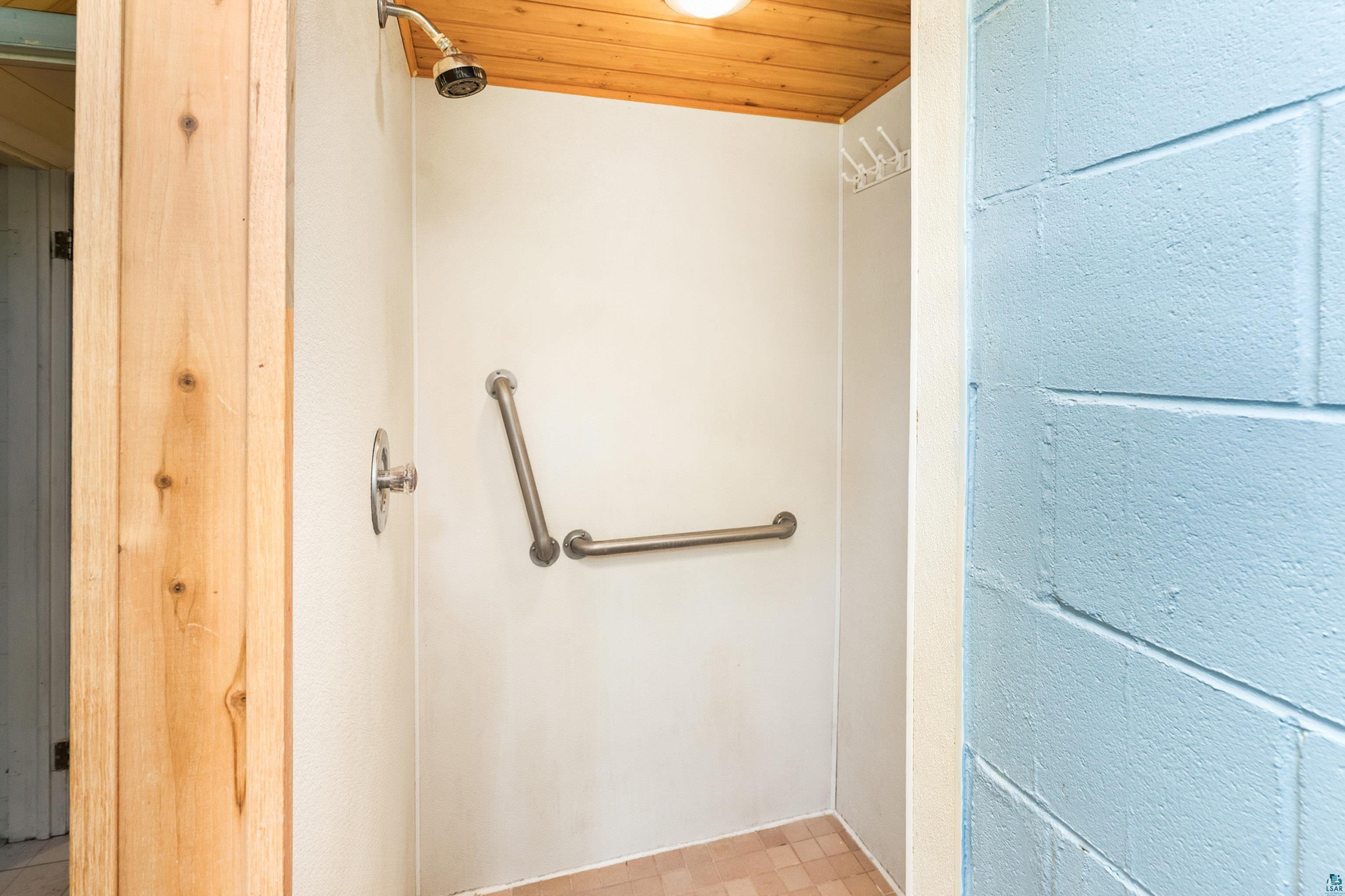 4808 Midway Road Duluth, MN 55811 - Photo 41 of 57 Walk-in shower featuring a wood-panel ceiling, brushed nickel showerhead, wall-mounted grab bars, and light-toned tile flooring