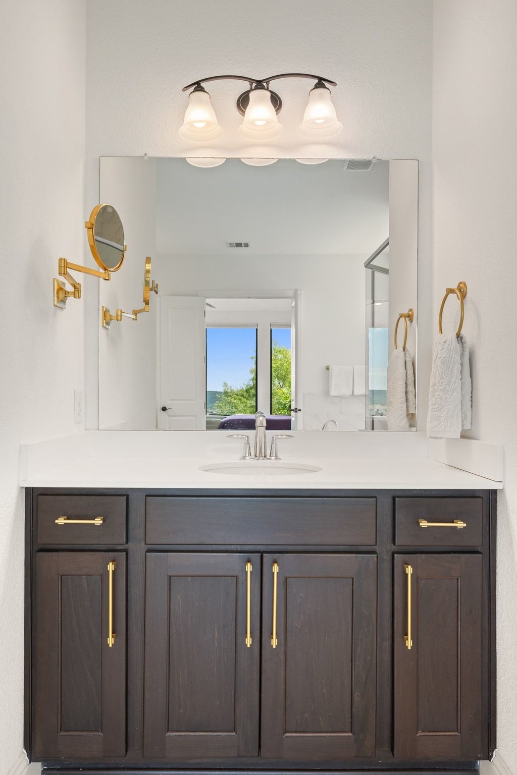 1221 Siena Sunset Road Leander, TX 78641 - Photo 24 of 39 Bathroom vanity featuring a dark wood-finish cabinet, gold-tone hardware, a white countertop, and an undermount sink with a chrome faucet