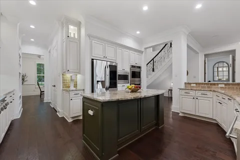 a kitchen with stainless steel appliances kitchen island granite countertop a stove a sink a refrigerator and white cabinets with wooden floor