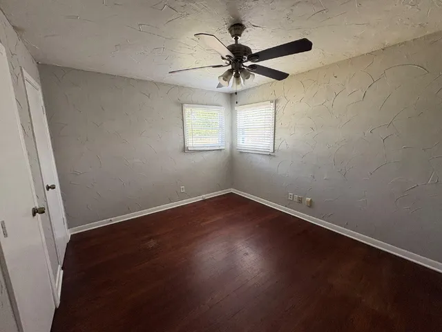 an empty room with wooden floor fan and windows