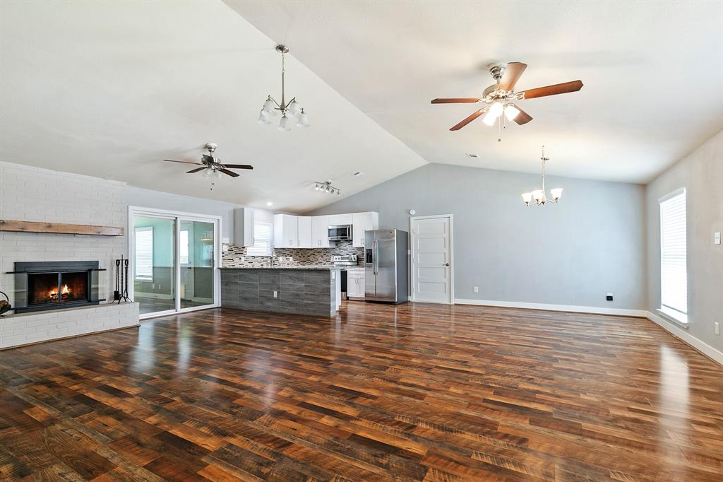 909 North Dove Road Grapevine, TX 76051 - Photo 15 of 30 Open-concept living space featuring wood-finish flooring, a white brick fireplace with a wood mantle, and vaulted ceilings