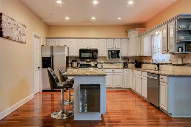 a kitchen with kitchen island granite countertop a stove top oven a sink dishwasher and a refrigerator with wooden floor