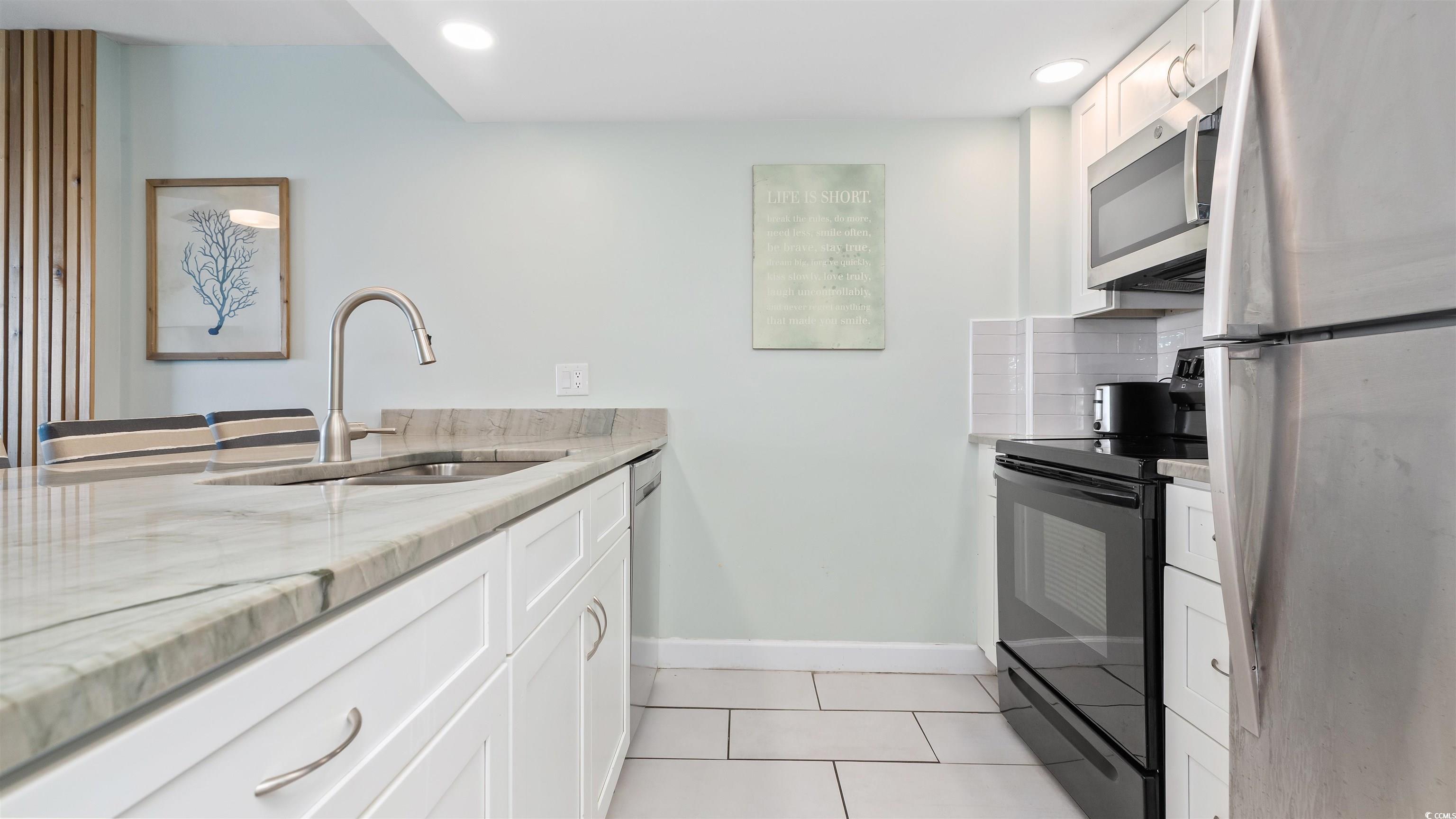 2001 South Ocean Boulevard, Unit 603 Myrtle Beach, SC 29577 - Photo 21 of 33 Kitchen with white cabinetry, appliances with stainless steel finishes, light tile patterned floors, light stone counters, and tasteful backsplash