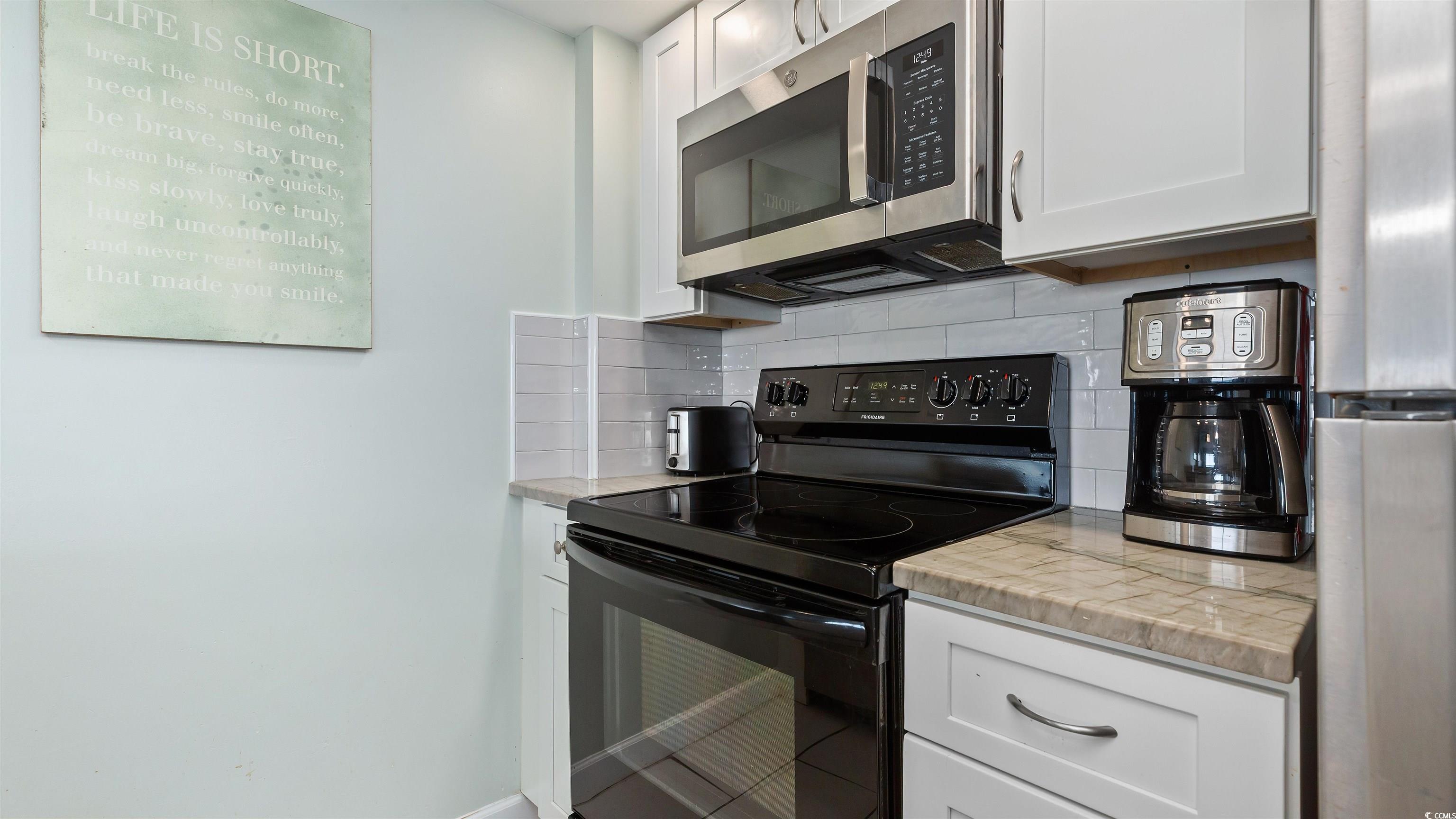 2001 South Ocean Boulevard, Unit 603 Myrtle Beach, SC 29577 - Photo 23 of 33 Kitchen with appliances with stainless steel finishes, white cabinets, light countertops, and tasteful backsplash