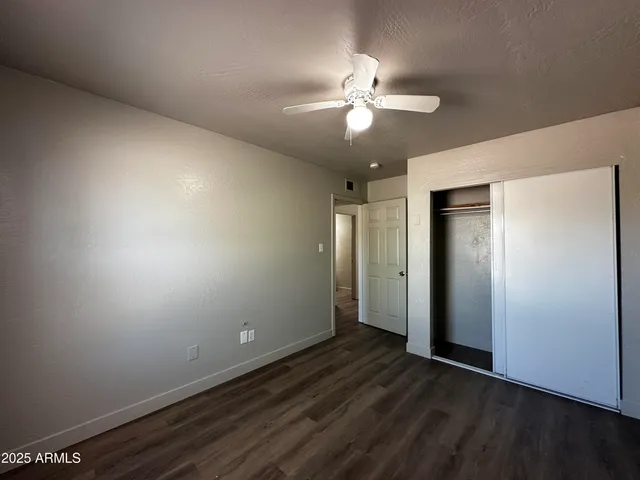 an empty room with wooden floor closet and fan