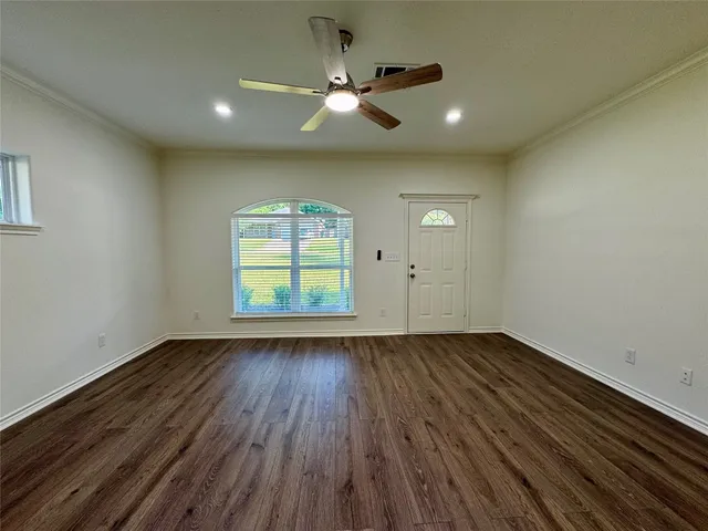 an empty room with wooden floor chandelier fan and windows