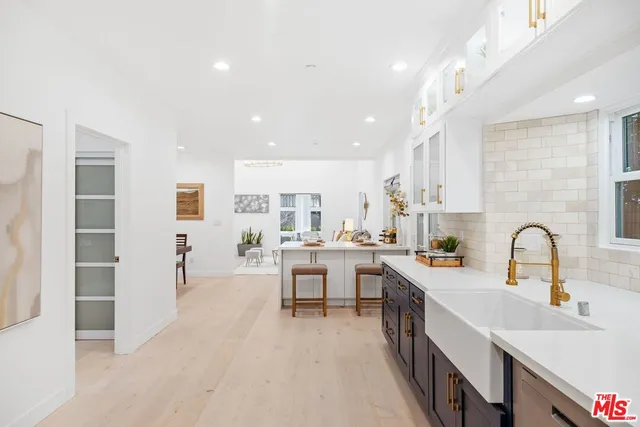 a large white kitchen with stainless steel appliances a sink a counter top space and cabinets