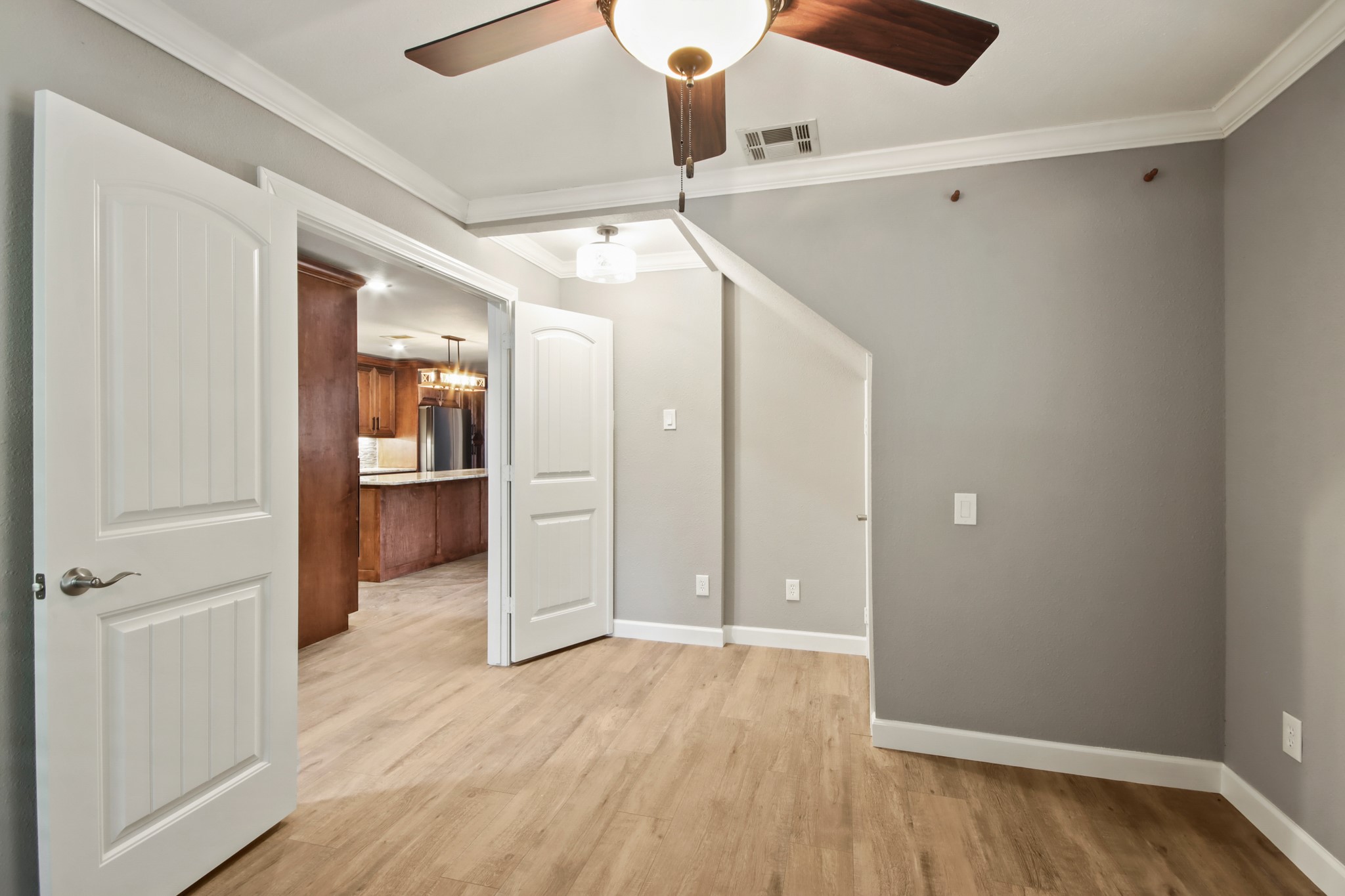 35 Susan Drive Cleveland, TX 77327 - Photo 14 of 33 This room features light wood flooring, neutral gray walls, and white trim. A ceiling fan with wooden blades is installed overhead. The space opens to a kitchen area with warm wood cabinetry and modern appliances.