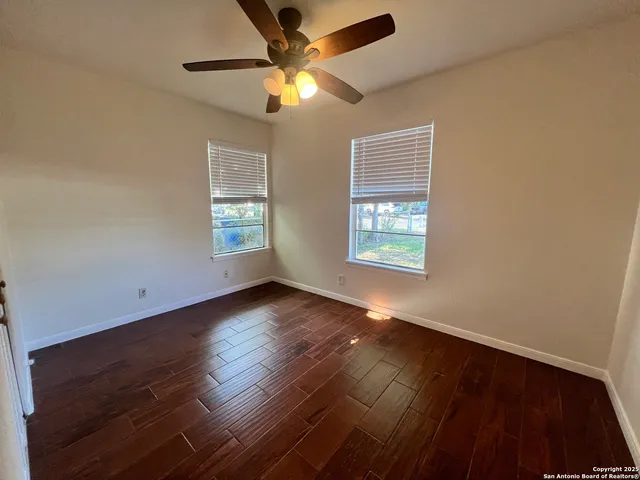 an empty room with wooden floor chandelier fan and windows