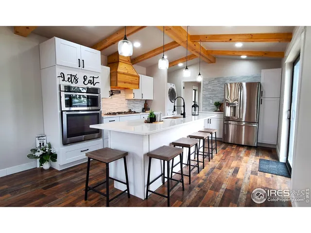 a kitchen with stainless steel appliances kitchen island granite countertop a refrigerator a stove a sink and white cabinets with wooden floor