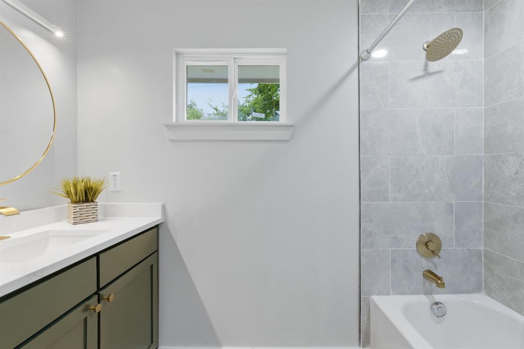 507 Country Club Road Cleburne, TX 76033 - Photo 24 of 39 Bathroom featuring a vanity with a white countertop, gold-toned fixtures, a built-in tub, and tiled shower surround