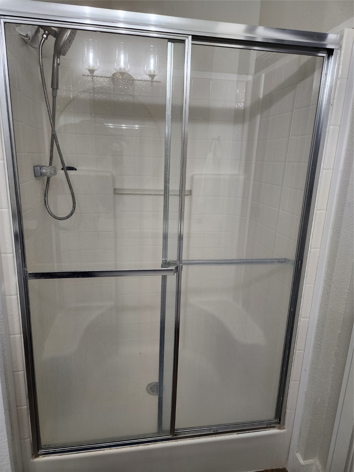 1491 Pecan Valley Road Wharton, TX 77488 - Photo 16 of 38 Experience a sleek, white-tiled shower with elegant sliding glass doors and a versatile detachable showerhead, perfect for a compact yet functional bathroom.