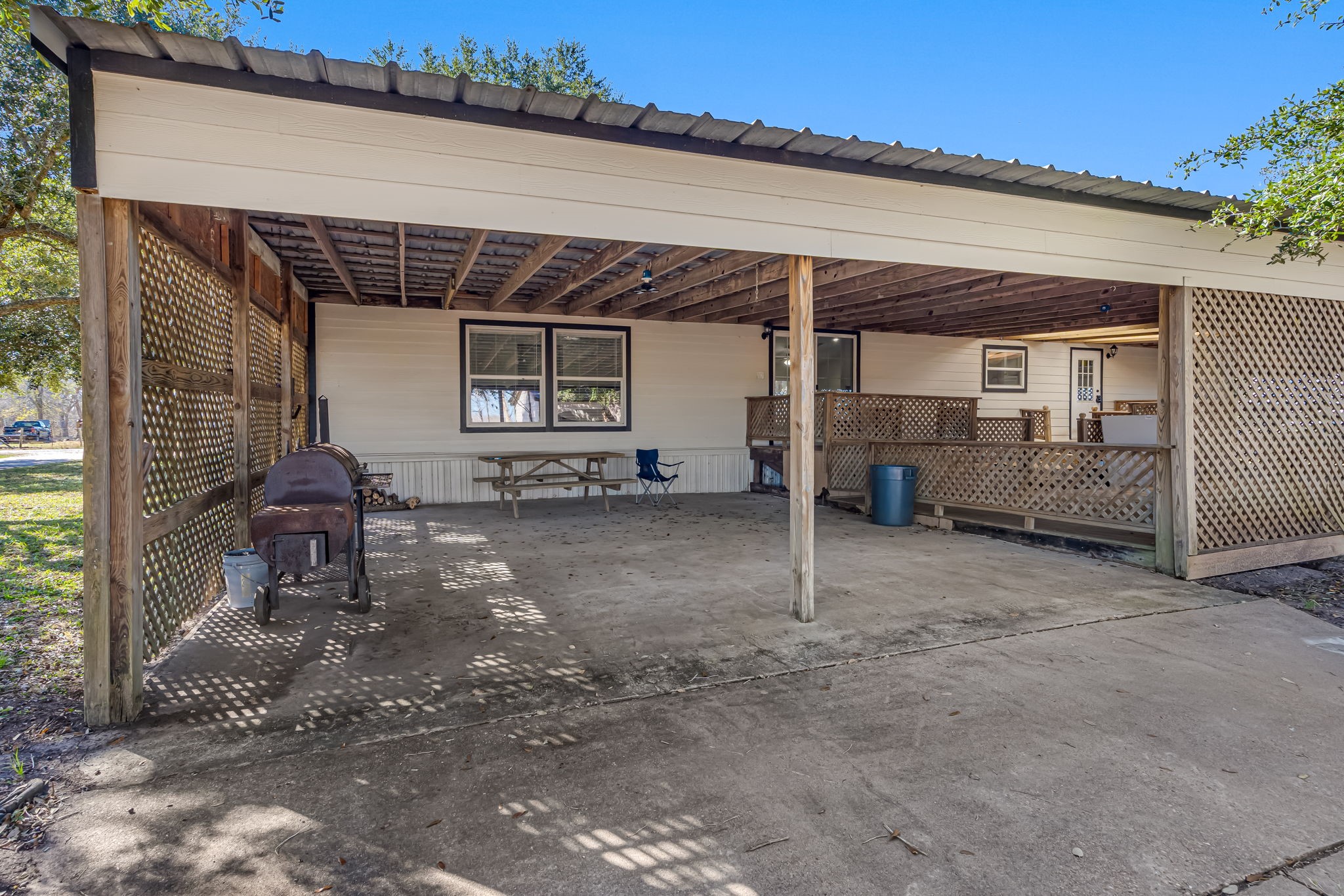 1491 Pecan Valley Road Wharton, TX 77488 - Photo 25 of 38 Spacious covered carport with lattice privacy panels, concrete floor, and a grill—perfect for outdoor gatherings and vehicle protection.