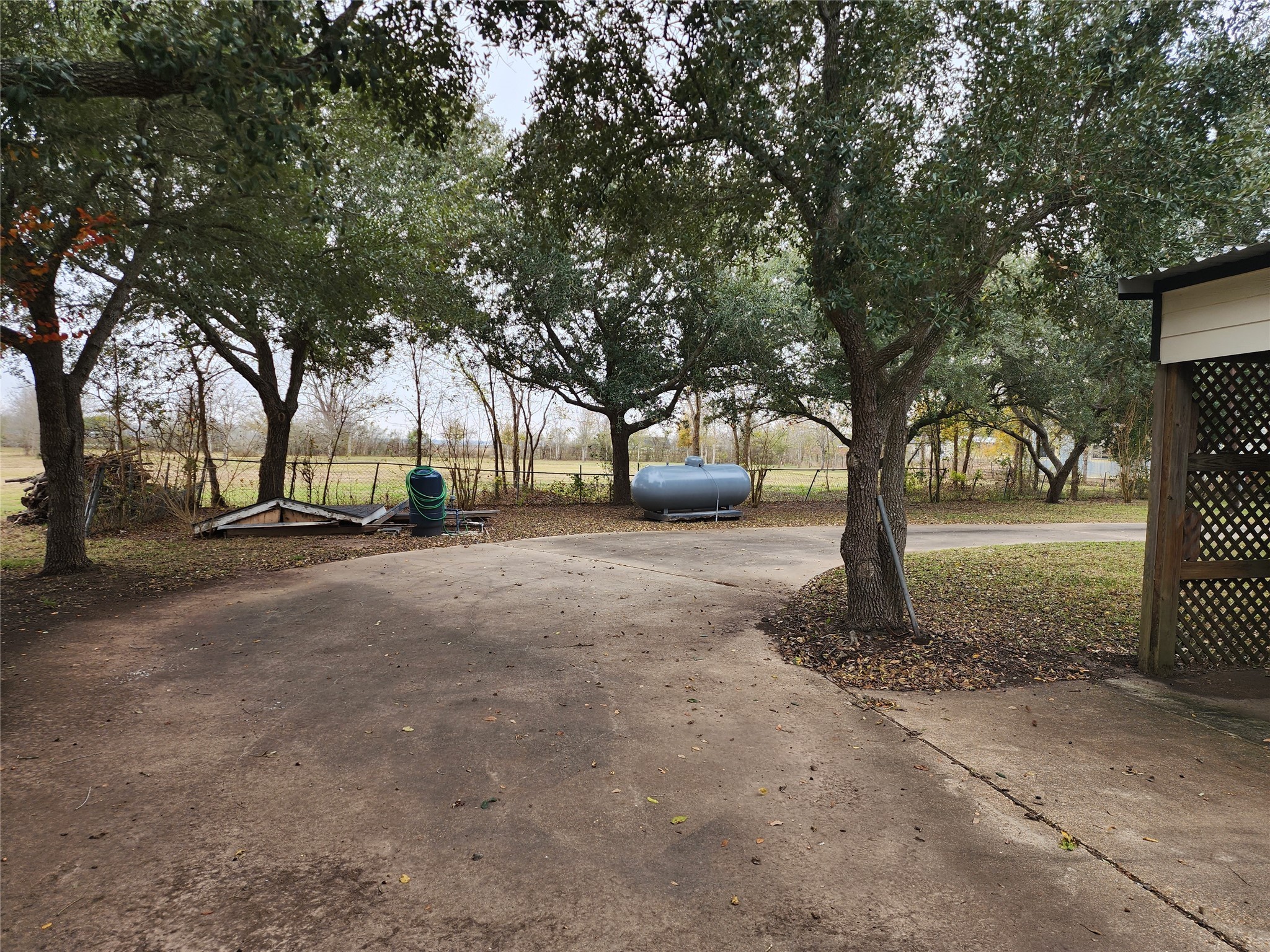 1491 Pecan Valley Road Wharton, TX 77488 - Photo 27 of 38 Spacious driveway with mature trees offering shade, a propane tank, and a partially hidden structure, creating a private, rustic ambiance.