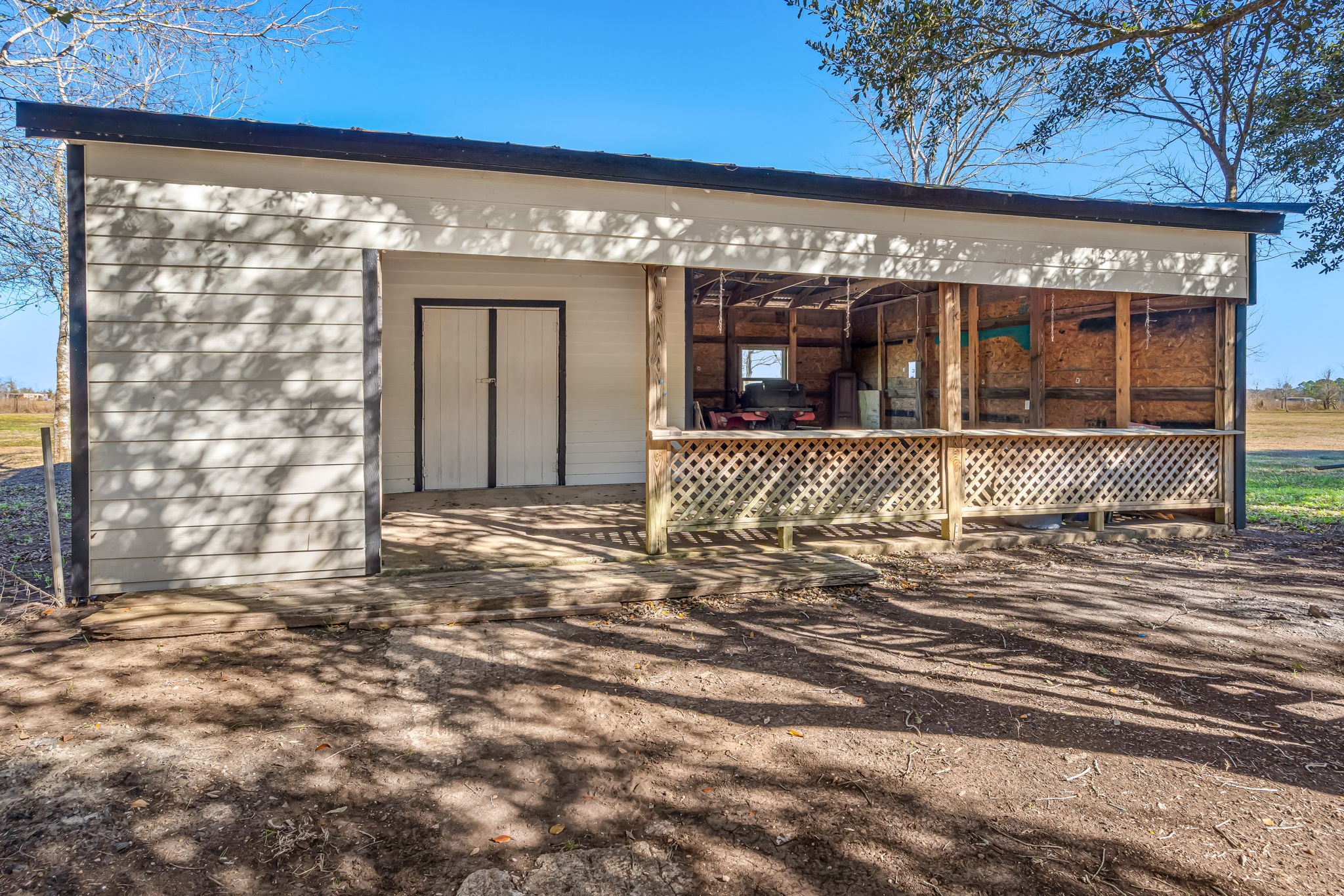 1491 Pecan Valley Road Wharton, TX 77488 - Photo 32 of 38 Charming rustic outbuilding with a weathered metal roof and wooden lattice porch, set in a spacious yard with mature trees. Perfect for storage or a workshop.