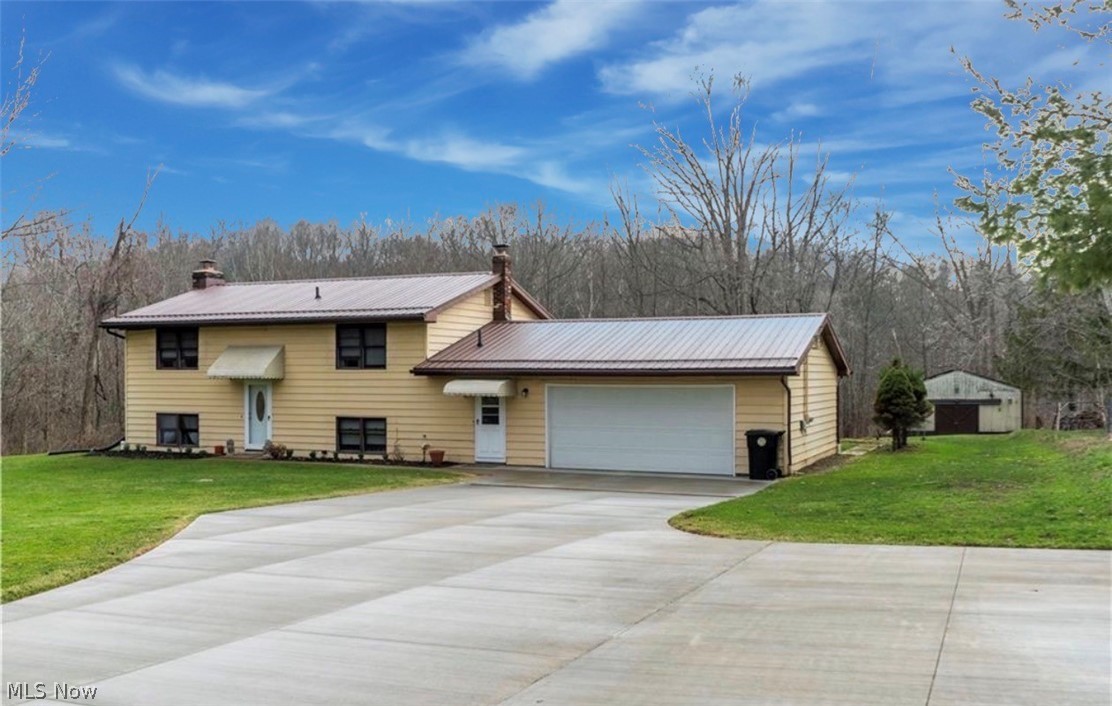 871 South County Line Road Geneva, OH 44041 - Photo 2 of 20 View of front of property featuring a front yard, a chimney, a metal roof, driveway, and an attached garage