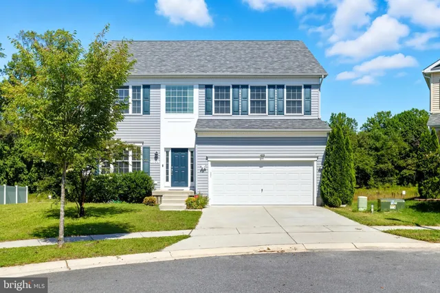a small yard in front of a white house with a large tree
