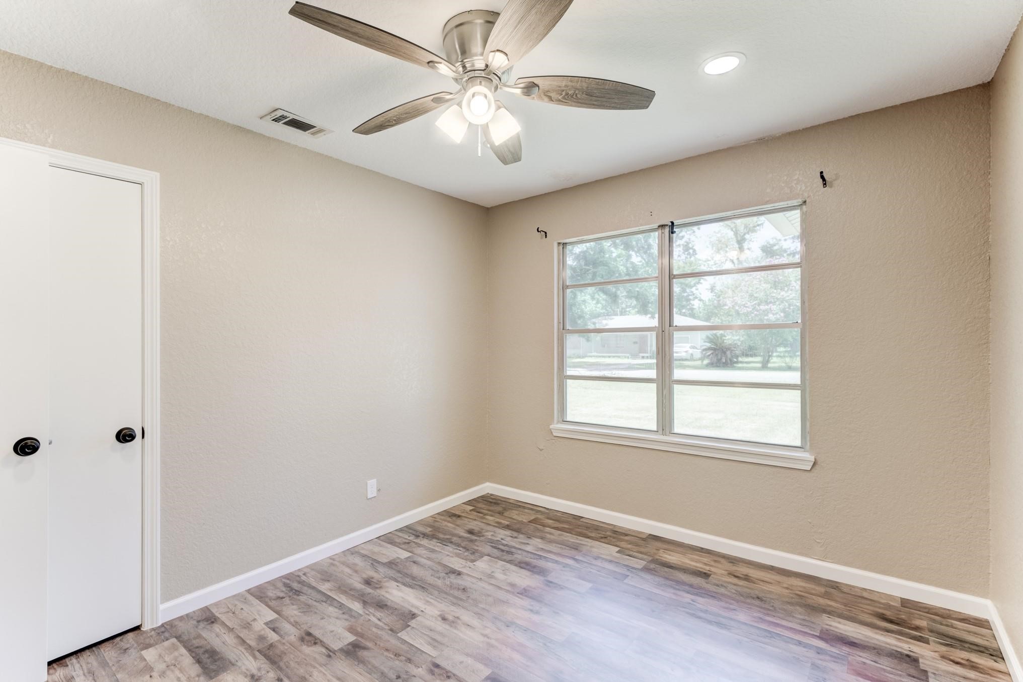 305 Yaupon Street Sweeny, TX 77480 - Photo 4 of 22 This room features neutral walls and wood-style flooring, creating a warm and welcoming atmosphere. It has a ceiling fan with lights and a large window that offers plenty of natural light and a pleasant view. A closet with white doors provides storage space.