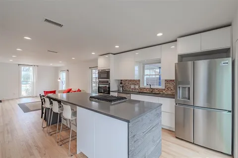a kitchen with stainless steel appliances granite countertop a refrigerator a sink a stove and white cabinets with wooden floor