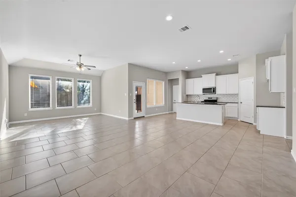 a view of an empty room with kitchen and window