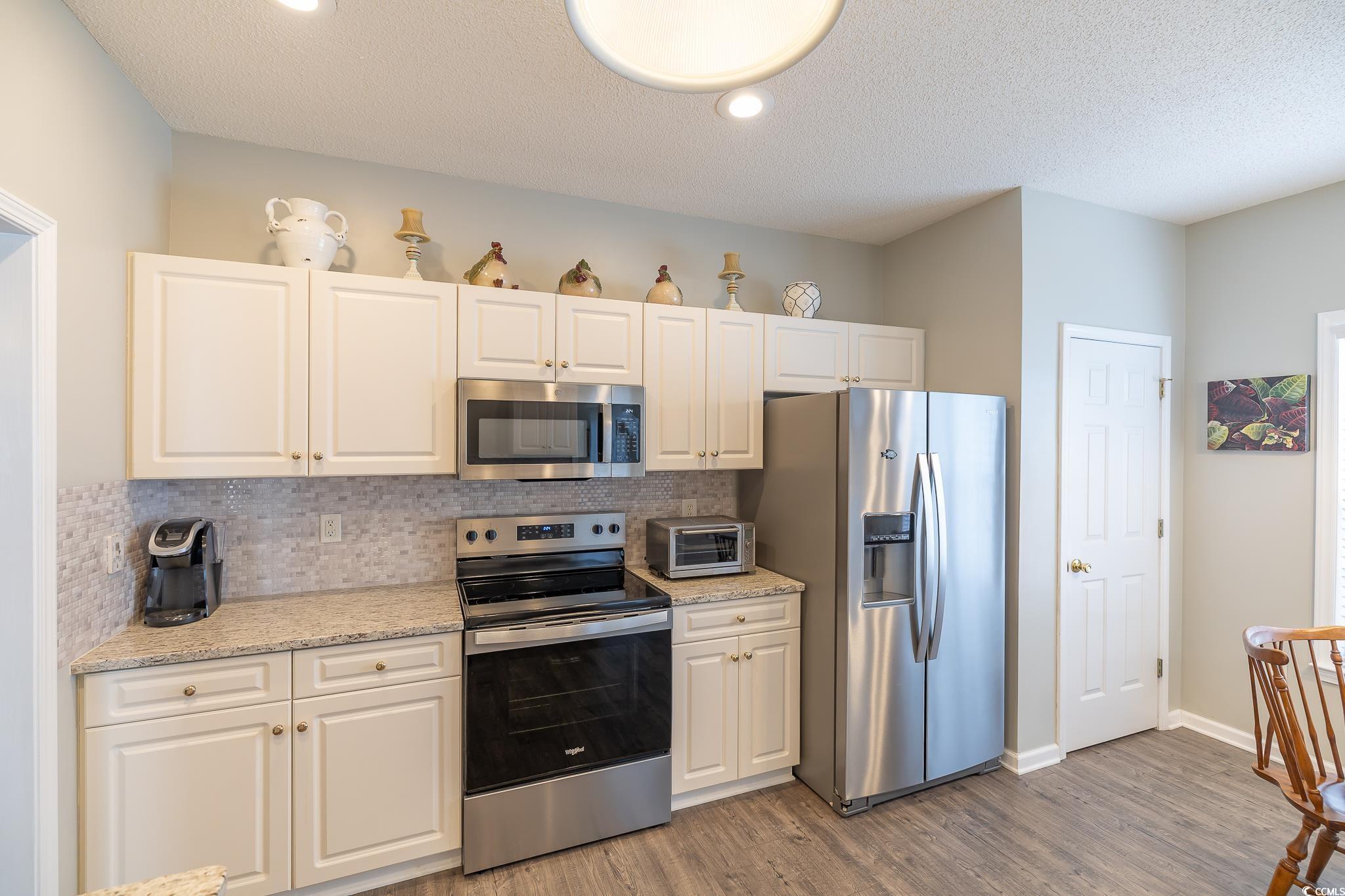 5077 Capulet Circle Myrtle Beach, SC 29588 - Photo 21 of 27 Kitchen with appliances with stainless steel finishes, decorative backsplash, light stone counters, white cabinetry, and a textured ceiling