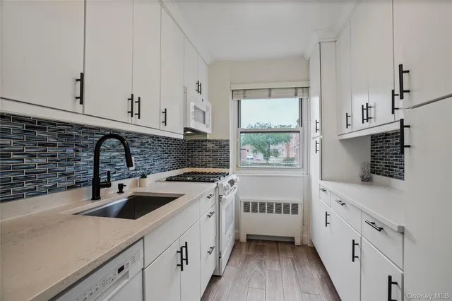 a kitchen with white cabinets a sink and a stove with wooden floor