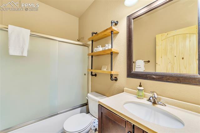 1055 Timber Ridge Road Divide, CO 80814 - Photo 25 of 47 Bathroom featuring vanity, a textured wall, toilet, and bath / shower combo with glass door