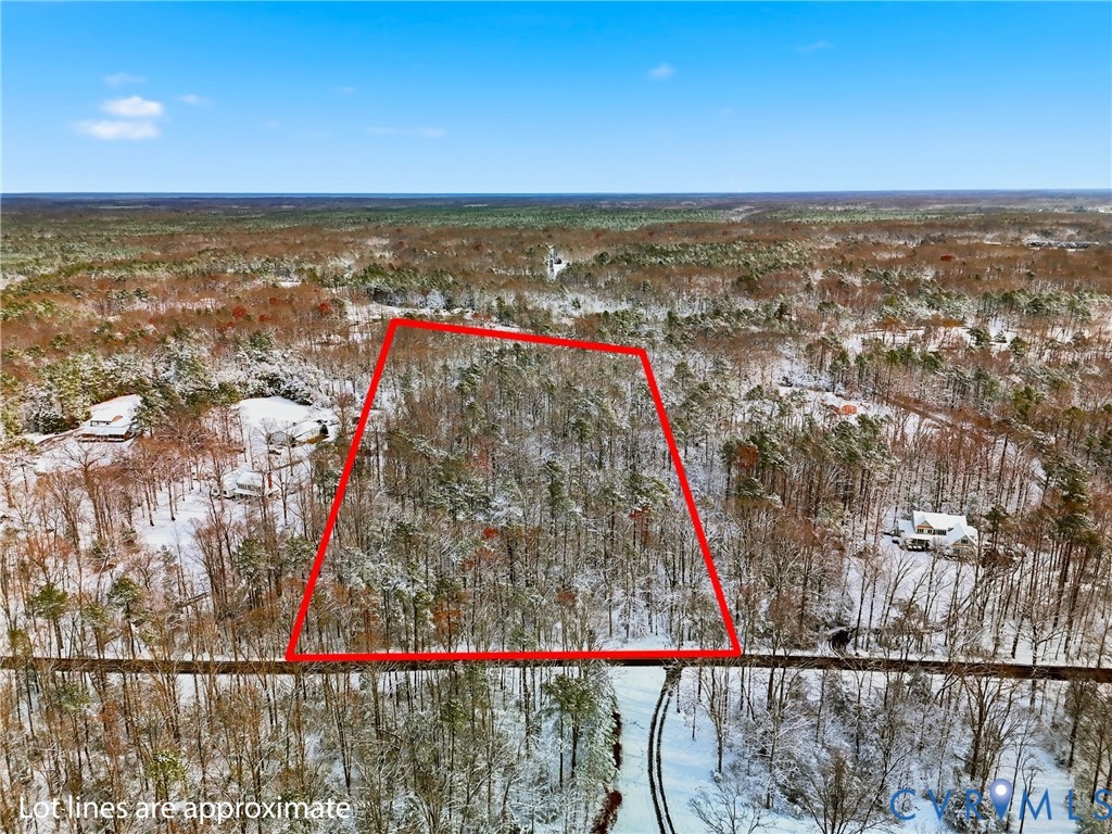 Snowy aerial view with a wooded view and property