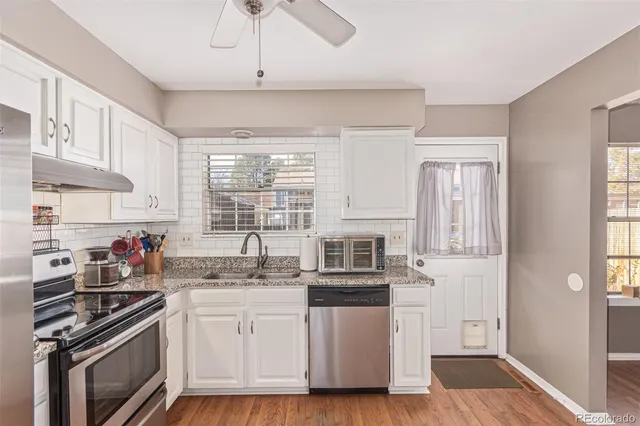 a kitchen with stainless steel appliances a stove a sink dishwasher a refrigerator white cabinets and wooden floor