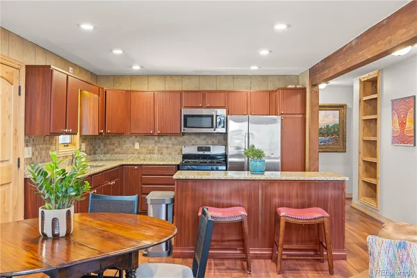 a kitchen with stainless steel appliances granite countertop a stove top oven a sink a refrigerator with a dining table and chairs